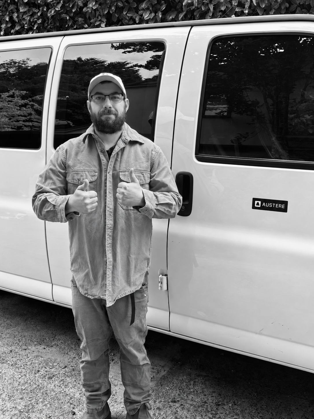 Black-and-white portrait of a man giving two thumbs up beside a van